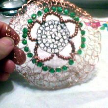 Load image into Gallery viewer, The kippah is held against a white tablecloth on which there  are some embroidered flowers.