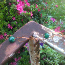 Load image into Gallery viewer, The copper and green headpiece is on a railing with pink flowers and green vines  in the background