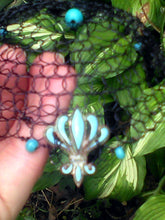 Load image into Gallery viewer, Closeup of black beaded wire kippah with turquoise beading and charm, being held against a backdrop of green  and white leaves.