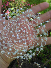 Load image into Gallery viewer, The crystal and pearl kippah is shwon  from the underside, on a hand. Grass and pink flowers are in the background.