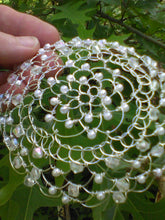 Load image into Gallery viewer, Crystal and pearl beaded wire kippah for woman.The kippah is being held against a background of green leaves.