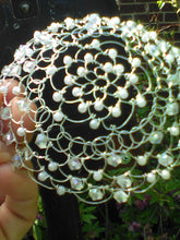 Load image into Gallery viewer, Crystal and pearl beaded silver wire kippah for woman. The kippah is being held, and in the background there is a black mailbox. Vines and flowers are at the bottom of the picture, near a brick wall.