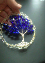 Load image into Gallery viewer, Silver and blue tree of life kippah or yarmulke, being held against a black background. A clear comb is attached.
