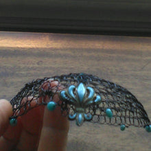 Load image into Gallery viewer, Black beaded wire kippah with turquoise beading and  fleur -de-lis charm, held in front of a brown table.