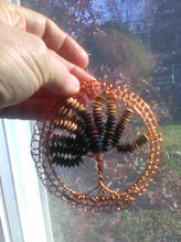 Load image into Gallery viewer, Bright copper wire supports wooden beads upoccled froma broken bracelet. Shown held againt a window, with autumn trees n the background.
