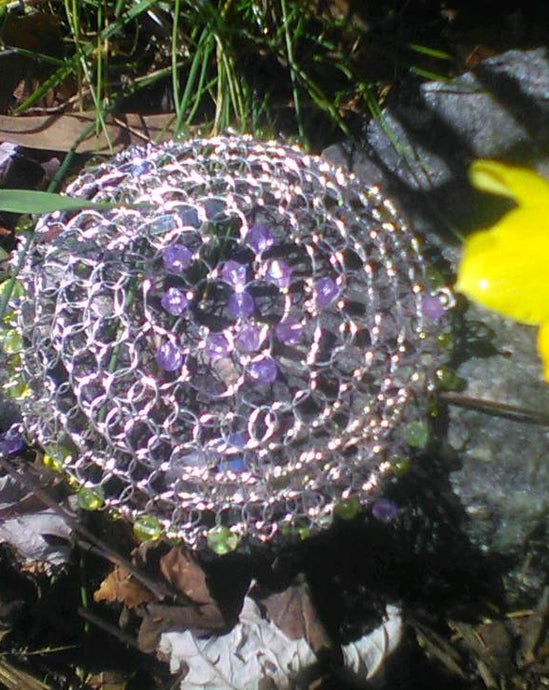 Purple and green crystals and beading on silver wire with a daffodil in the foreground and grass in the backgound