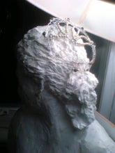 Load image into Gallery viewer, The silver, black and gold TOL rests on a sculpture; thee is a lampshade in the top of the picture
