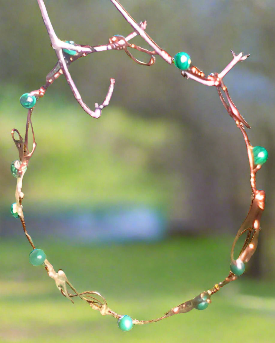 Green ,possibly malachite beads form the olives on this copper olive branch circlet, which is shown hanging in a tree.