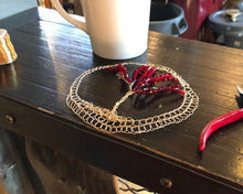 Load image into Gallery viewer, Ruby Red TOL kippah shown on dark wood with spool of gold wire and wire tool. A  white coffee cup is also on the wooden counter, and there is an industrial coffee grinder in the background.
