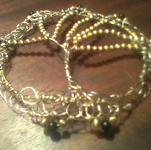 Load image into Gallery viewer, The kippah is resting on a wooden background. It is made from siver and gold wire, with gold and black beads repurposed from necklaces. About 4.5 inches circumference.
