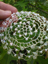Load image into Gallery viewer, Crystal and pearl beaded wire kippah for woman.The kippah is being held against a background of green leaves.
