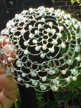 Load image into Gallery viewer, Crystal and pearl beaded silver wire kippah for woman. The kippah is being held, and in the background there is a black mailbox. Vines and flowers are at the bottom of the picture, near a brick wall.
