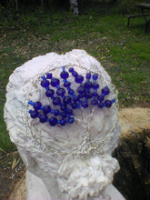 Load image into Gallery viewer, A silver and blue tree of life kippah on the bust of a woman&#39;s head. A tree trunk is visible in the foreground and there is an angel sculpture in the garden. 
