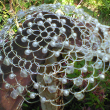 Load image into Gallery viewer, Crystals and pearls in abundance on silver wire kippah. The kippah is shown on a railing, wth green leaves in the background.
