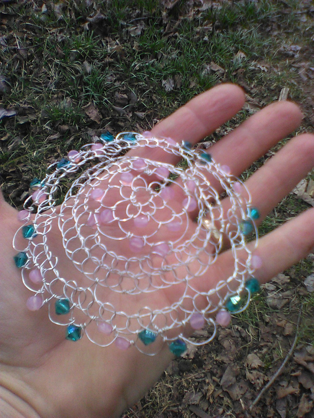 Teal and pink beaded silver wire kippah. The kippah is on a hand to show the size.